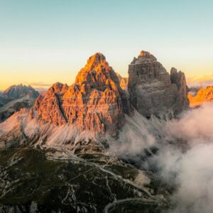 The Tre Cime di Lavaredo peaks glowing at sunrise, with fog nestled in the valley.