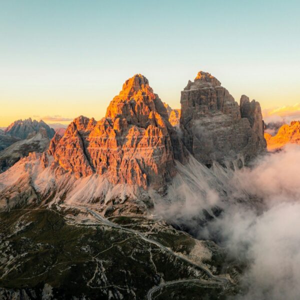 The Tre Cime di Lavaredo peaks glowing at sunrise, with fog nestled in the valley.