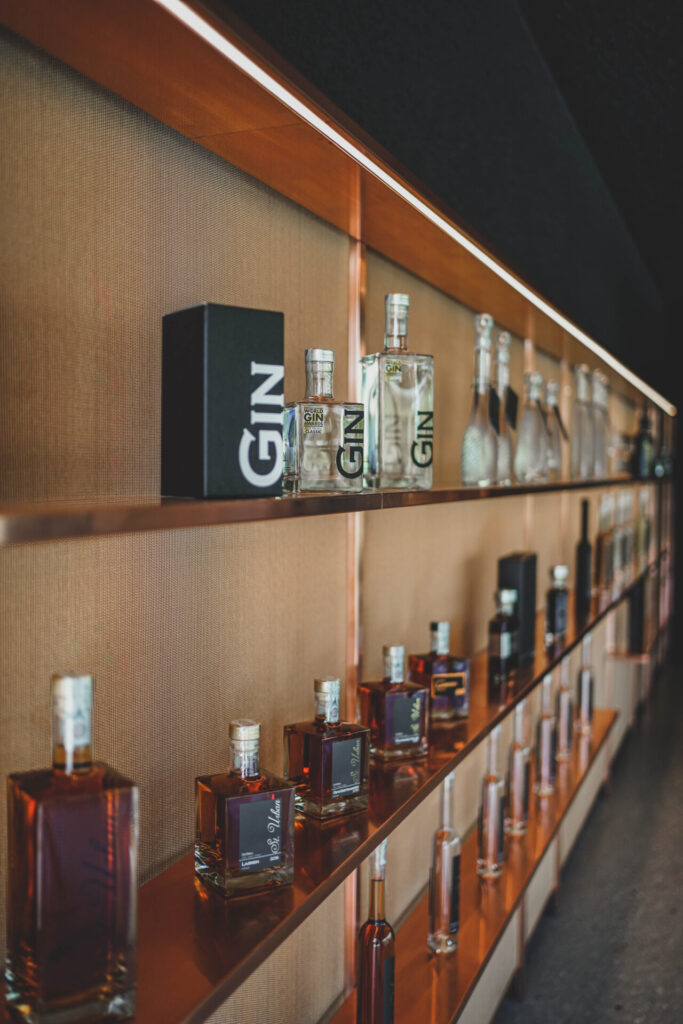 Display shelves hold various gin and spirit bottles and boxes against textured bronze backdrop.