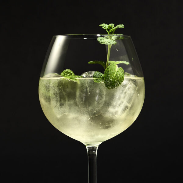 Tall wine glass filled with an iced, bubbly drink and garnished with fresh mint sprigs against a black background.