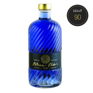 A bottle of 'Blue Tea Gin' with a gold cap, a textured blue surface, and a Falstaff 90 label.
