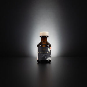 Bottle of Munakra Handcrafted Gin with a label of flowers and a wooden top sits on a reflective surface.